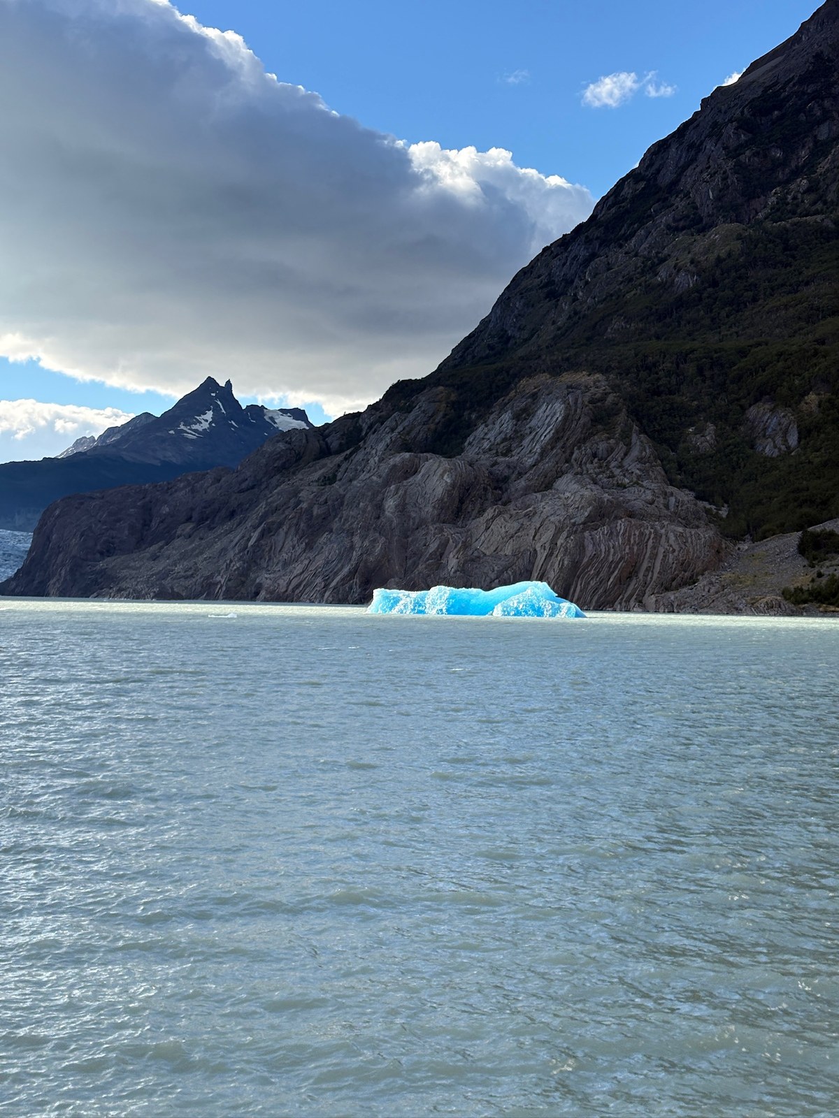 A blue iceberg beneath mountains and a dramatic sky